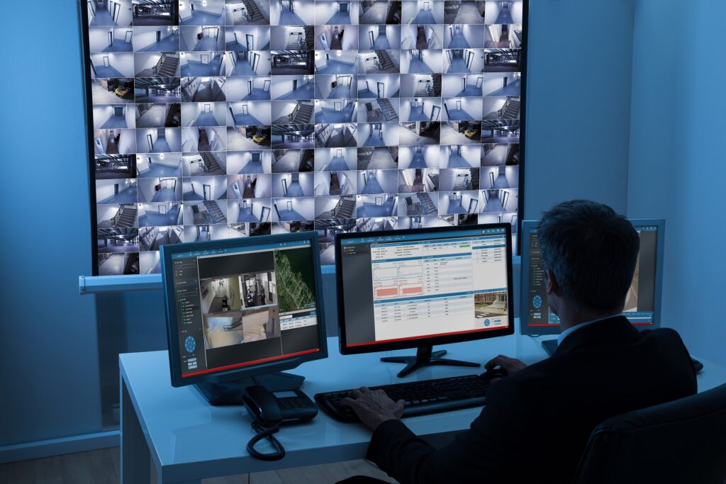 Rear View Of A Man In Control Room Monitoring Multiple Cctv Footage