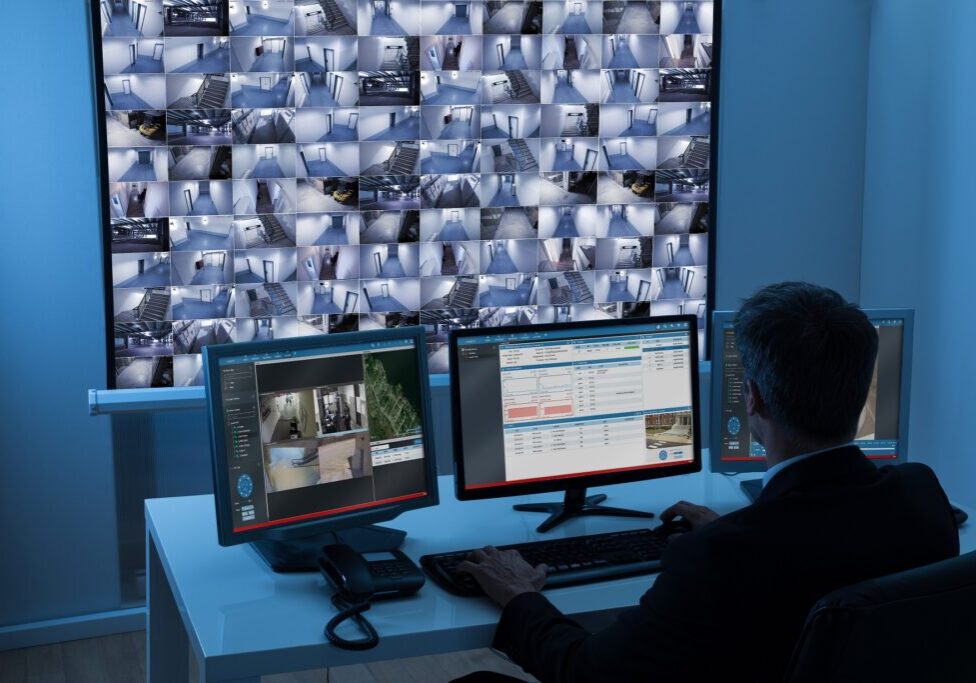 Rear View Of A Man In Control Room Monitoring Multiple Cctv Footage